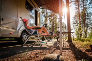 person lounging in a chair under a motorhome awning, RV setup at a campsite, at sunset